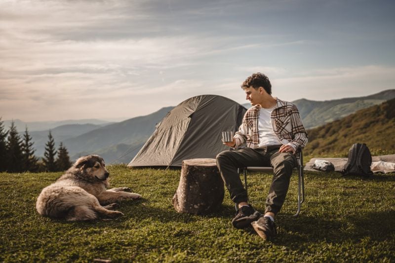 Zelt reinigen: Ein Mann sitzt mit seinem Hund vor seinem Zelt.