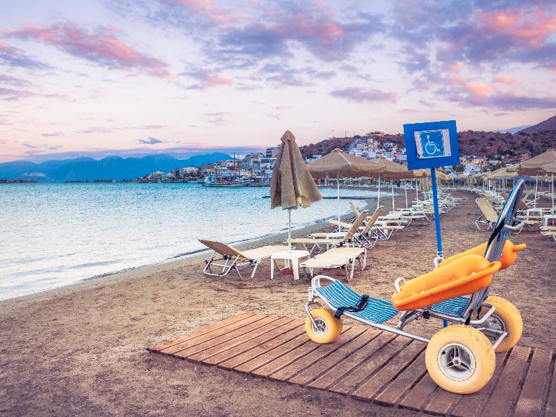 Strandrolstoel op het strand met strandbedjes op de achtergrond. 