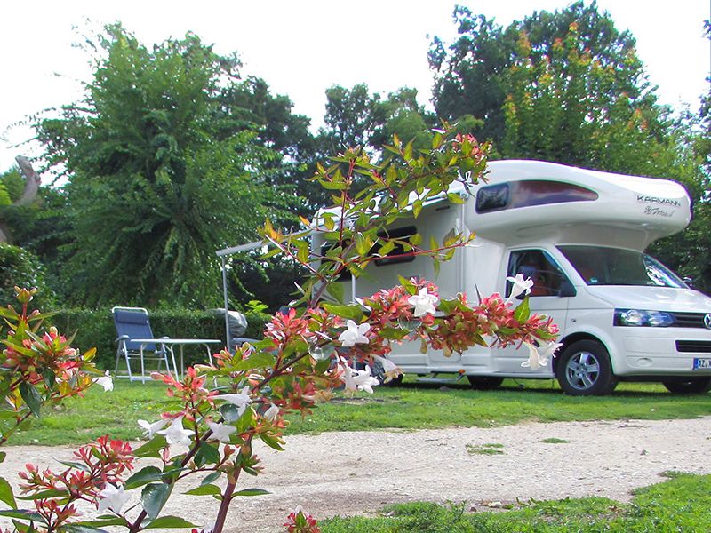 Camping La Poterie: camper en klapstoelen met tafel. Takken met roze en witte bloemen op de voorgrond.