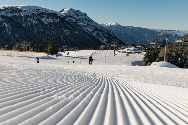 Präparierte Skipisten im Val di Fiemme mit Blick auf die umliegenden Dolomiten an einem sonnigen Wintertag