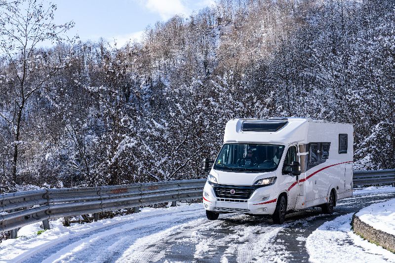 Camper op besneeuwde bergweg in Italië in de winter, onderweg in alpiene regio met beperkte toegang