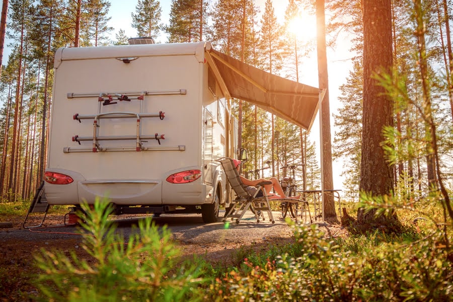 kampeerder in stoel voor camper in een bosrijke omgeving