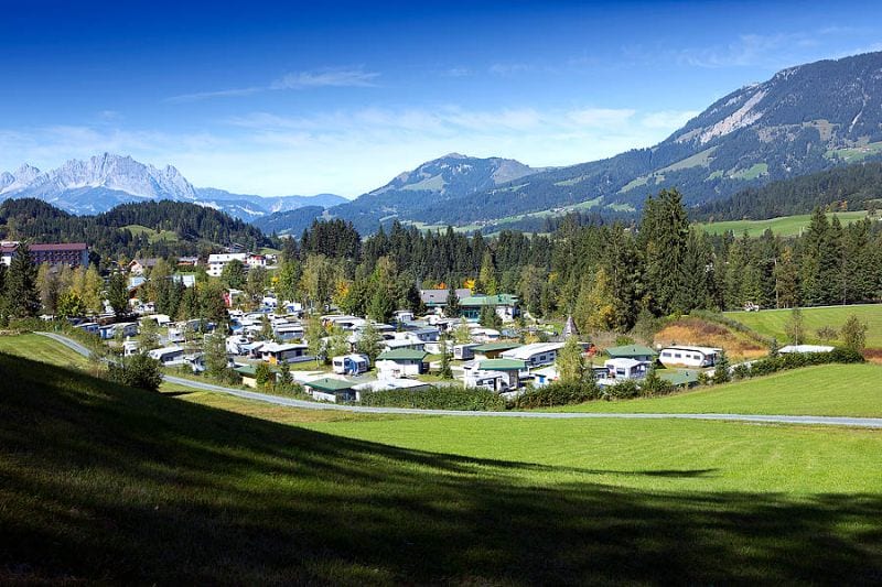 Overzicht van Tirol Camp in een groene vallei met caravans en campers, omringd door bergen en bossen in Oostenrijk