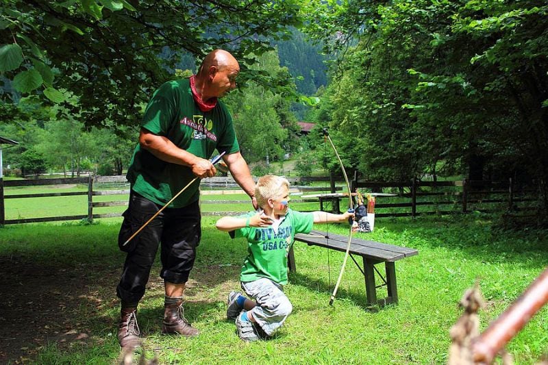 Man helpt kind met boogschieten op een groene camping bij Komfort-Campingpark Burgstaller in Oostenrijk