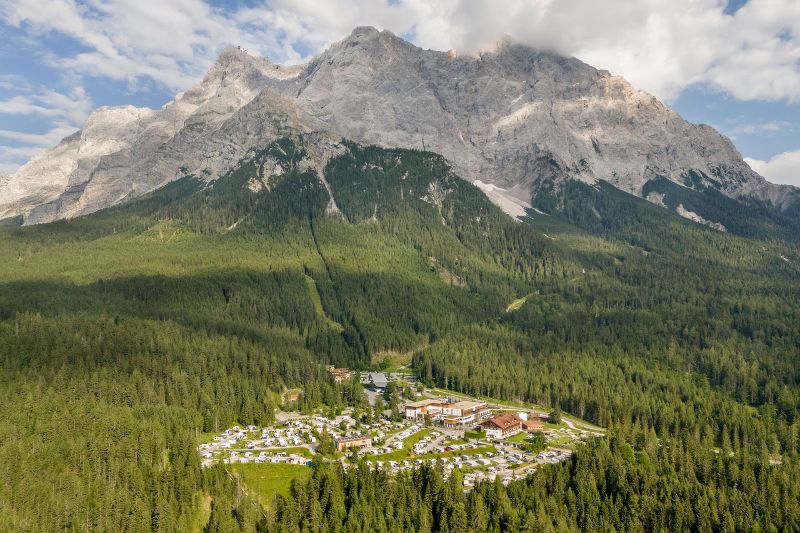Luchtfoto van Zugspitz Resort Camping aan de voet van een imposante berg, omringd door dicht bos in Oostenrijk