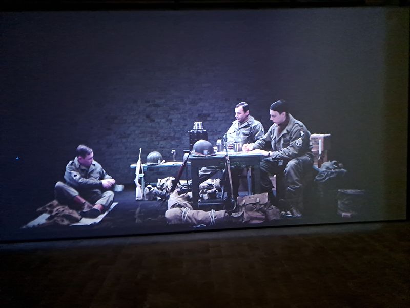 Levensgrote projectie in het Bastogne War Museum van Amerikaanse soldaten tijdens de Slag om de Ardennen. De militairen zitten rond een tafel met kaarten en uitrusting, als onderdeel van een interactieve tentoonstelling over de Tweede Wereldoorlog.